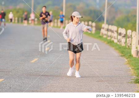Active Asian woman checking her smartwatch while jogging in the park. Female runner tracking heart rate and progress during outdoor fitness workout. Wearable technology and healthy lifestyle concept Active Asian woman checking her smartwatch while jogging in the park. Female runner tracking heart rate and progress during outdoor fitness workout. Wearable technology and healthy lifestyle concept 139546215