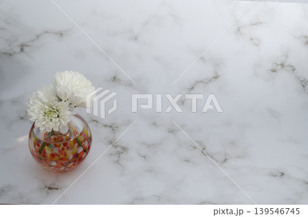 明るい背景で暖色硝子球形一輪挿に白色い菊(左配置) 139546745
