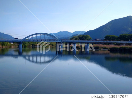 穏やかな川面に映る橋と山並みの静かな水辺風景 穏やかな川面に映る橋と山並みの静かな水辺風景 139547074