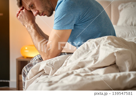 Stressed man sitting on bed with clasped hands 139547581