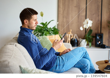 Man using smartphone while sitting on sofa at home Man using smartphone while sitting on sofa at home 139547604