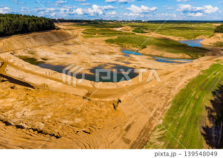 Expansive sand quarry, a major open-pit mine, revealing significant earthworks and water pockets, set against a distant urban backdrop 139548049