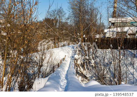Serene snowy footpath bridging a winter ravine, sunlight glinting on pristine snow, surrounded by dormant trees under a crisp blue sky. Idyllic frosty walk Serene snowy footpath bridging a winter ravine, sunlight glinting on pristine snow, surrounded by dormant trees under a crisp blue sky. Idyllic frosty walk 139548537
