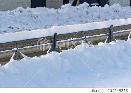 Metal guardrail heavily laden with pristine white snow drifts against a backdrop of winter landscape and cleared roadway Metal guardrail heavily laden with pristine white snow drifts against a backdrop of winter landscape and cleared roadway 139549258