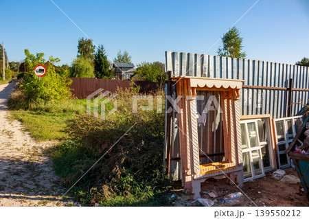 Ornate wooden window casing and old frames lean against a corrugated fence in a rustic village. Rural construction debris or discarded architectural elements 139550212