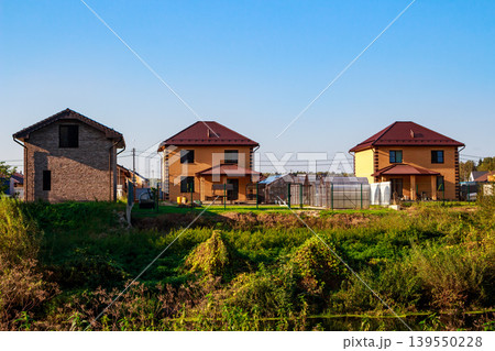 Modern suburban homes with vibrant gardens and greenhouses under a clear blue sky, hinting at tranquil country living Modern suburban homes with vibrant gardens and greenhouses under a clear blue sky, hinting at tranquil country living 139550228
