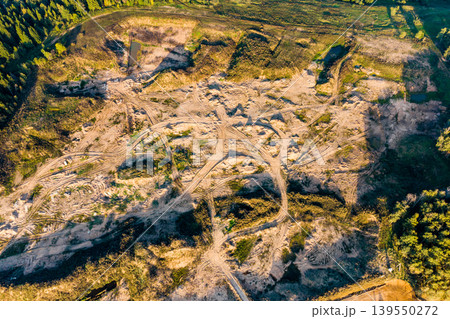 Active sand quarry aerial view. Numerous vehicle tracks crisscross the sandy landscape. Green forest surrounds this industrial site, showcasing resource extraction Active sand quarry aerial view. Numerous vehicle tracks crisscross the sandy landscape. Green forest surrounds this industrial site, showcasing resource extraction 139550272