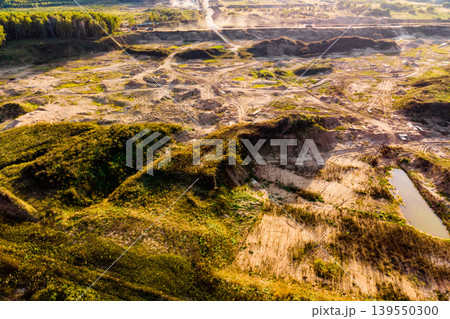 Aerial view of an active quarry landscape with earthworks and heavy machinery creating a vast, industrial scene under golden light, showcasing human impact on nature Aerial view of an active quarry landscape with earthworks and heavy machinery creating a vast, industrial scene under golden light, showcasing human impact on nature 139550300