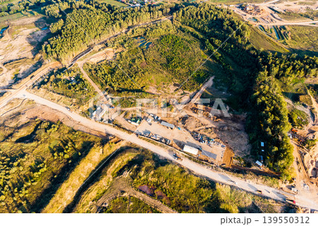 Aerial shot of a new quarry under construction. Roads, buildings, and earthmoving equipment are visible on cleared land amidst green hills. Busy industrial development Aerial shot of a new quarry under construction. Roads, buildings, and earthmoving equipment are visible on cleared land amidst green hills. Busy industrial development 139550312