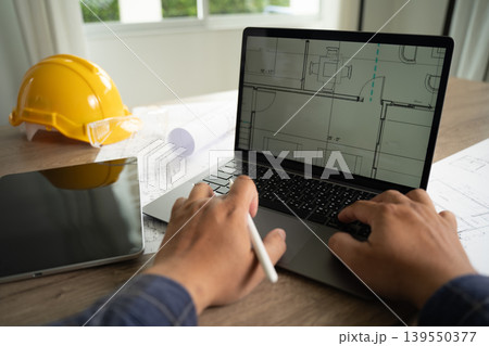 Hands using laptop displaying architectural blueprint with stylus and devices on desk, representing AI assisted design workflow, engineering data analysis process, digital modeling, and construction Hands using laptop displaying architectural blueprint with stylus and devices on desk, representing AI assisted design workflow, engineering data analysis process, digital modeling, and construction 139550377