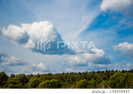 Majestic, billowy clouds drift across a vibrant blue expanse, with a lush forest and green trees grounding the view below. Nature's beauty Majestic, billowy clouds drift across a vibrant blue expanse, with a lush forest and green trees grounding the view below. Nature's beauty 139550447