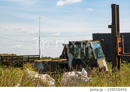 An old, rusty, abandoned forklift truck sits in an overgrown field under a bright sky. This vintage industrial hulk, a forgotten workhorse, shows signs of decay An old, rusty, abandoned forklift truck sits in an overgrown field under a bright sky. This vintage industrial hulk, a forgotten workhorse, shows signs of decay 139550450