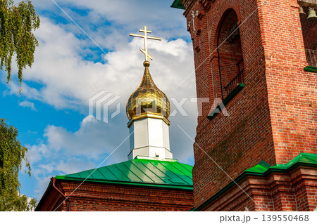 Glimmering gold orthodox cupola and cross atop a rustic brick church against a vivid sky with fluffy clouds Glimmering gold orthodox cupola and cross atop a rustic brick church against a vivid sky with fluffy clouds 139550468