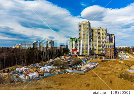 Striking aerial drone shot of slick new residential towers in progress, with a bustling building site. Urban sprawl unfolding near woodlands under a vivid sky Striking aerial drone shot of slick new residential towers in progress, with a bustling building site. Urban sprawl unfolding near woodlands under a vivid sky 139550501