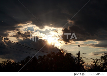 Majestic sunlight pierces through stormy clouds, creating a dramatic sky at dusk. Golden rays peek through dark, thick cumulonimbus Majestic sunlight pierces through stormy clouds, creating a dramatic sky at dusk. Golden rays peek through dark, thick cumulonimbus 139550502