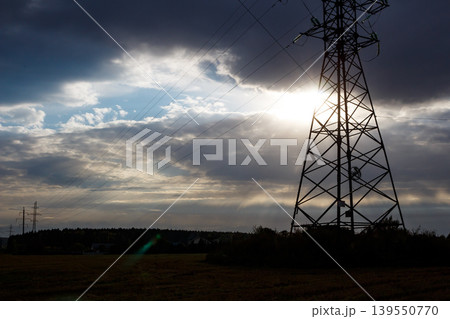 Dramatic silhouette of a power pylon against a vibrant sunset sky, sunrays piercing through energetic clouds. A powerful symbol of energy and modern infrastructure Dramatic silhouette of a power pylon against a vibrant sunset sky, sunrays piercing through energetic clouds. A powerful symbol of energy and modern infrastructure 139550770