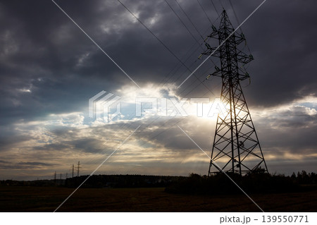 Monolithic pylon, a silent sentinel of power, silhouetted against a dramatic, sun-kissed, cloudy sky, connecting the world with vital energy lines Monolithic pylon, a silent sentinel of power, silhouetted against a dramatic, sun-kissed, cloudy sky, connecting the world with vital energy lines 139550771