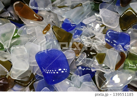 Vibrant, smooth tumbled glass shards mimic colorful sea glass. Frosted and clear, blue, green, amber pieces gleam in an attractive heap 139551185