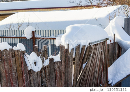 Rustic wooden fence heavily blanketed by fresh, glistening snow under bright winter sun. Old planks and posts are almost hidden by thick white drifts, creating a serene, cold landscape Rustic wooden fence heavily blanketed by fresh, glistening snow under bright winter sun. Old planks and posts are almost hidden by thick white drifts, creating a serene, cold landscape 139551331