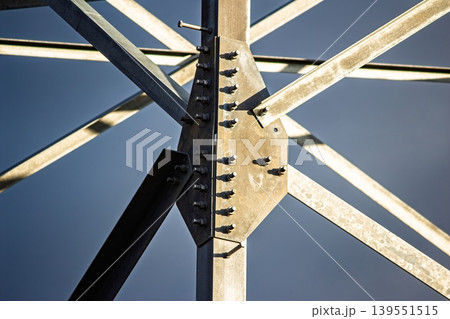 Robust steel lattice of an electricity pylon against a clear sky. Close-up of bolted metal beams, showcasing industrial strength and intricate engineering details Robust steel lattice of an electricity pylon against a clear sky. Close-up of bolted metal beams, showcasing industrial strength and intricate engineering details 139551515