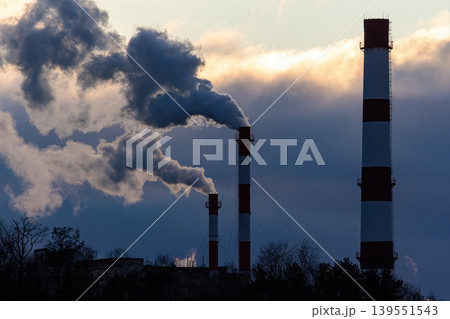 Industrial chimneys fiercely belch dense smoke into a dramatic, twilight sky. A powerful visual of environmental impact and energy production at dusk Industrial chimneys fiercely belch dense smoke into a dramatic, twilight sky. A powerful visual of environmental impact and energy production at dusk 139551543