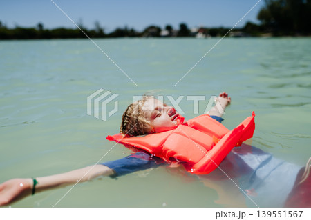 Child floating on water wearing life jacket during summer day. Child floating on water wearing life jacket during summer day. 139551567