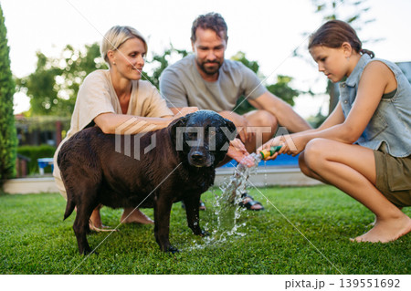 Parents and child cooling dog with water on sunny day. Parents and child cooling dog with water on sunny day. 139551692