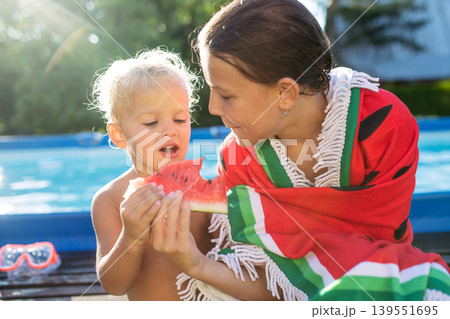 Sister and toddler brother eating watermelon after swimming in pool. 139551695