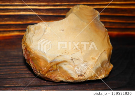 A roughly processed flint ax lying on a wooden background. Late Bronze Age, Russia 139551920