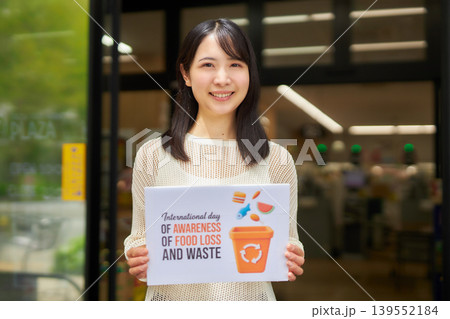 スーパーマーケットの前で食品ロスのプラカードを持つ若い女性 139552184