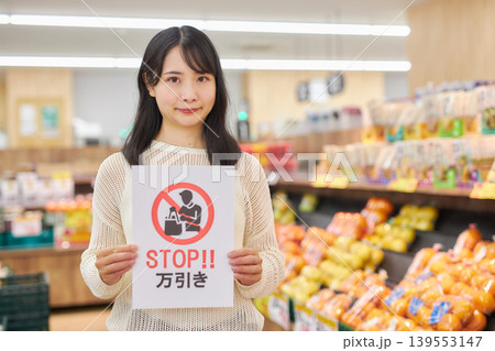 スーパーマーケットの商品の前で万引き防止のプラカードを持つ若い女性 スーパーマーケットの商品の前で万引き防止のプラカードを持つ若い女性 139553147