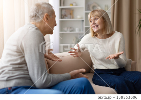 Mature couple sitting on sofa at home, both gesturing with open hands 139553606