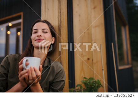Young woman with coffee outdoors, weekend away in container house in countryside. 139553627