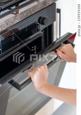 A hands open the door of a modern built-in oven. Concept of home cooking and appliance use. A hands open the door of a modern built-in oven. Concept of home cooking and appliance use. 139554168