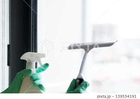 Washing the window with a gloved scraper and a spray bottle of detergent, removing water droplets  139554191