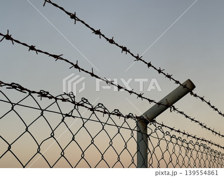 Barbed wire fence at sunset with a colorful sky, suitable for background or conceptual use Barbed wire fence at sunset with a colorful sky, suitable for background or conceptual use 139554861
