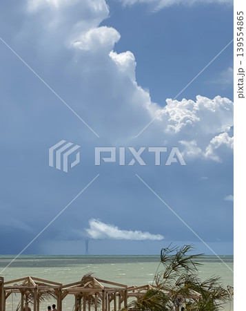 Cloudy sky over calm sea with wooden pergolas on sandy beach, ideal for relaxing summer background 139554865