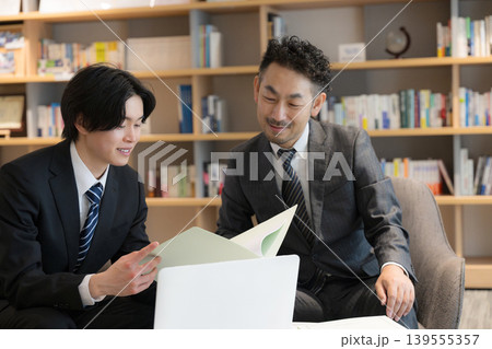 本棚背景でノートPCで打ち合わせする顧客の社長と若手のビジネスマン2人 提案や説明などの法人営業 本棚背景でノートPCで打ち合わせする顧客の社長と若手のビジネスマン2人 提案や説明などの法人営業 139555357
