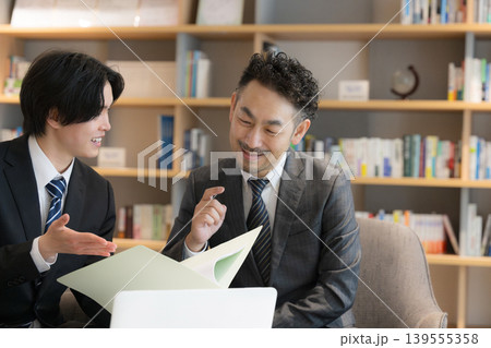 本棚背景でノートPCで打ち合わせする顧客の社長と若手のビジネスマン2人 提案や説明などの法人営業 本棚背景でノートPCで打ち合わせする顧客の社長と若手のビジネスマン2人 提案や説明などの法人営業 139555358