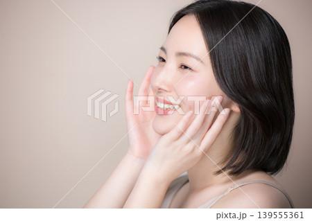 ベージュ背景で透明感で美肌に触れる笑顔の女性スキンケアと美容クローズアップイメージ横顔 ベージュ背景で透明感で美肌に触れる笑顔の女性スキンケアと美容クローズアップイメージ横顔 139555361