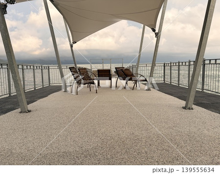 Wooden chairs are arranged along a concrete pier overlooking the sea 139555634