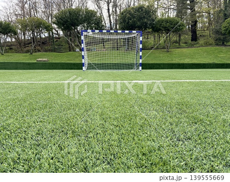 a bright, well-maintained soccer field covered in vibrant green artificial turf. Soccer goal featuring a white net and posts painted with blue and white vertical stripes. a bright, well-maintained soccer field covered in vibrant green artificial turf. Soccer goal featuring a white net and posts painted with blue and white vertical stripes. 139555669