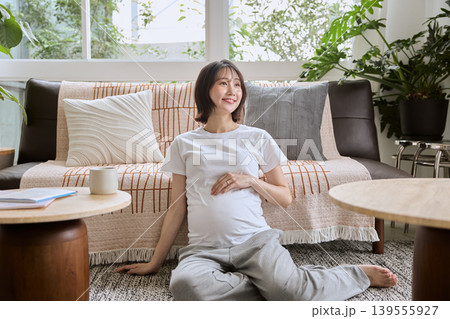 リビングの床に座りお腹に手を当てる笑顔の妊婦 139555927