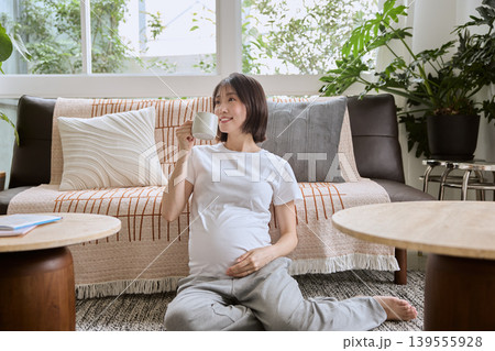 リビングの床に座りカップを持つ笑顔の妊婦 リビングの床に座りカップを持つ笑顔の妊婦 139555928