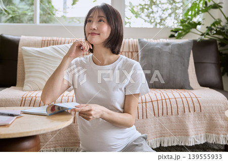 リビングのソファに座り本を読みながら考え事をする妊婦 リビングのソファに座り本を読みながら考え事をする妊婦 139555933
