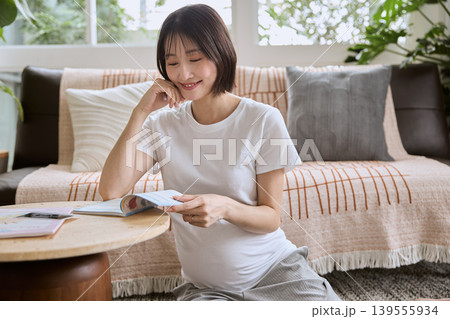 リビングでくつろぎながら本を読む妊婦の女性 リビングでくつろぎながら本を読む妊婦の女性 139555934