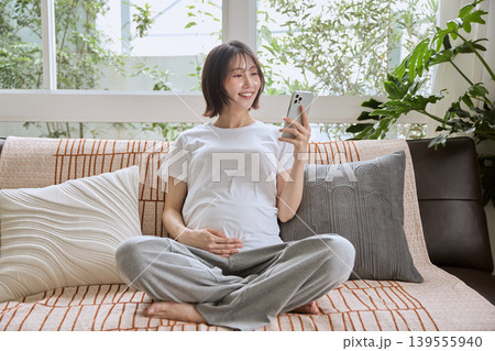 ソファでスマートフォンを見る笑顔の妊婦 ソファでスマートフォンを見る笑顔の妊婦 139555940