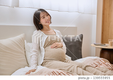 ベッドでお腹に手を当てて微笑む妊婦の女性 ベッドでお腹に手を当てて微笑む妊婦の女性 139555955