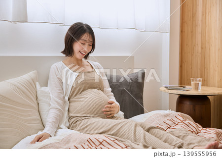 ベッドでお腹に手を当てて微笑む妊婦 ベッドでお腹に手を当てて微笑む妊婦 139555956