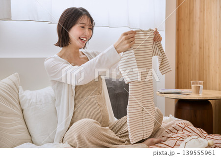 ベビー服を手に持ち笑顔で眺める妊婦 139555961